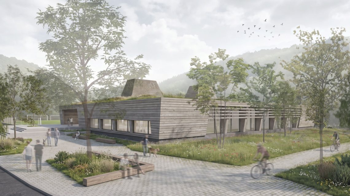 Stadthalle Schelklingen: kompakter Holzbau mit begrüntem Dach und zwei Licht- und Luftdomen, davor ein baumbestandener Vorplatz im Längental